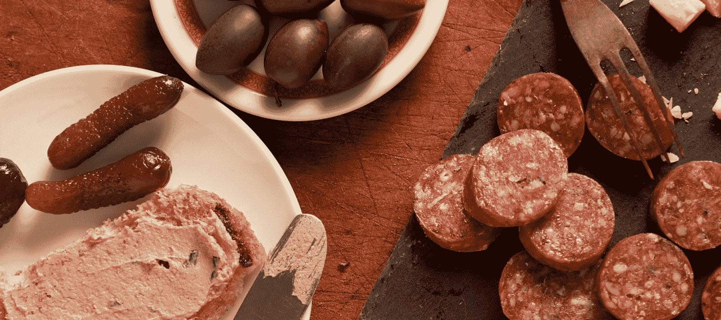 Sliced salami, olives, cornichons, and pate spread on bread