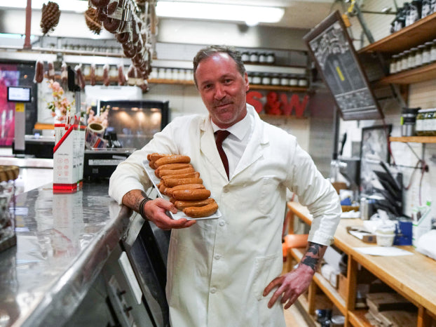 Jeremy Schaller holding sausages behind counter in Schaller & Weber butcher store