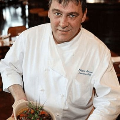 Phillip Roussel smiling at camera in white chef uniform holding a dish
